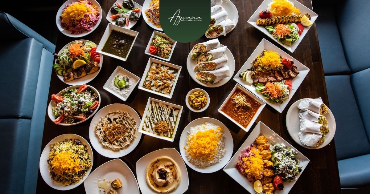 Large Persian serving platters with kebabs, rice, and shared dishes placed at the center of a group dining table