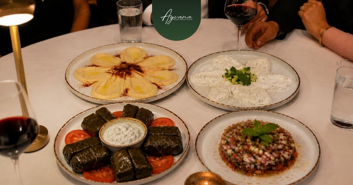 Persian appetizers including hummus, mast-o-khiar, shirazi salad, and dolmeh shared around a group dining table